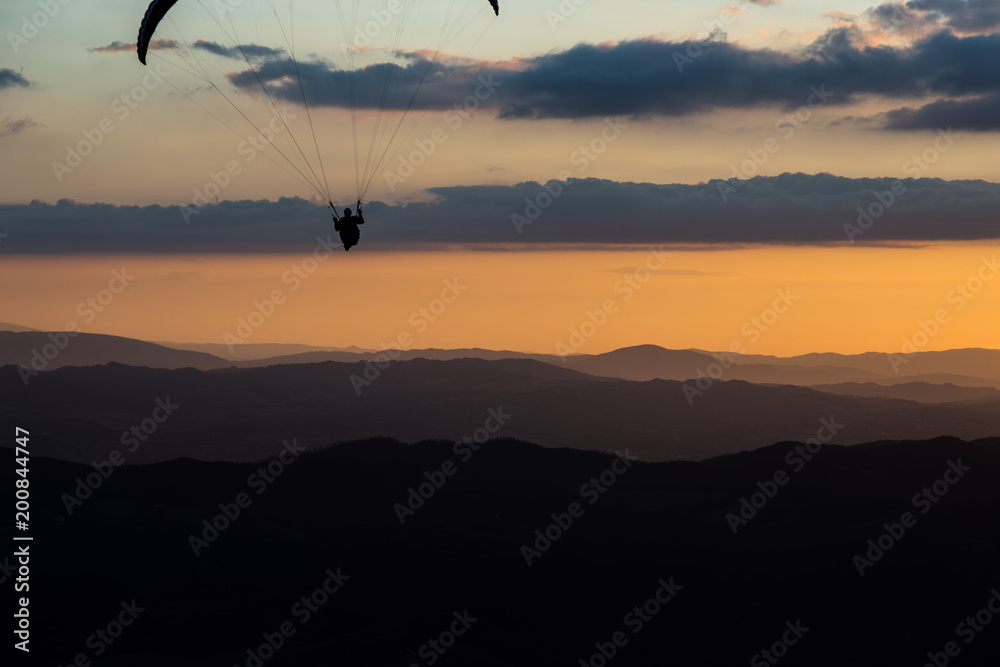 Beautiful shot of a paraglider silhouette flying over Monte Cucco (Umbria, Italy) with sunset on the background, with beautiful colors and dark tones