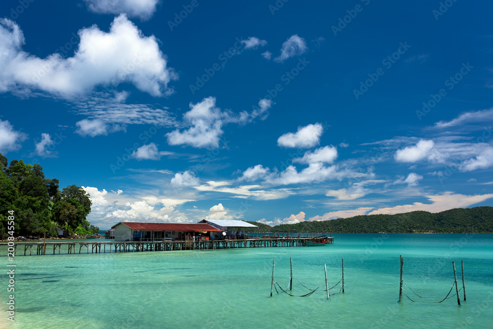 Tropical landscape of fisherman bay with turquoise clean water , pier in the distance and hammock on the beach.   Koh Rong Samloem. Cambodia, Asia.