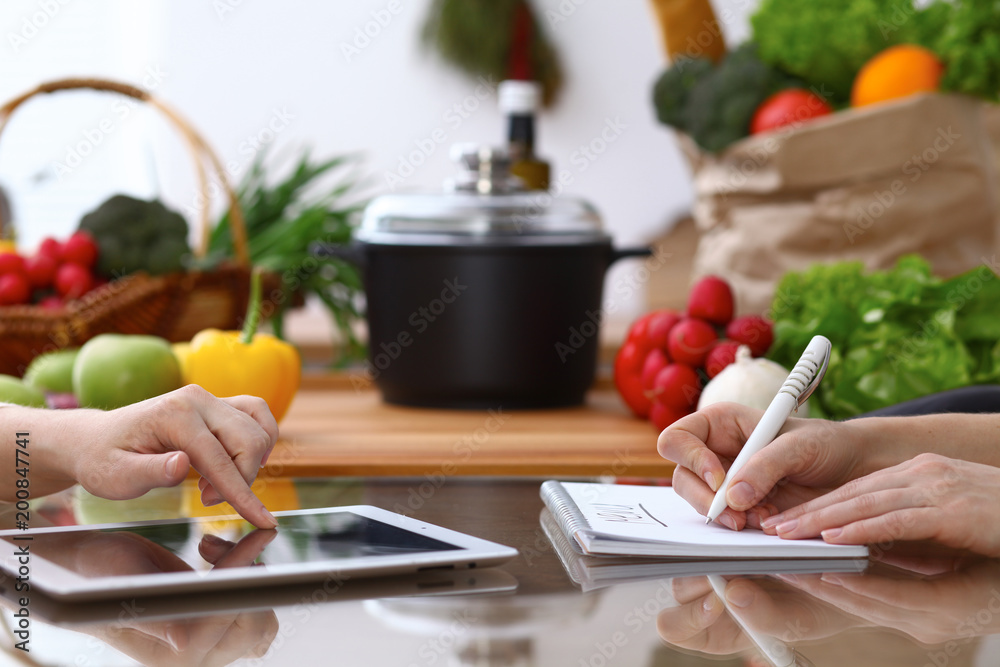 Closeup of human hands cooking in kitchen. Women discuss a menu using tablet computer. Copy space area at touch pad. Healthy meal, vegetarian food and lifestyle concepts