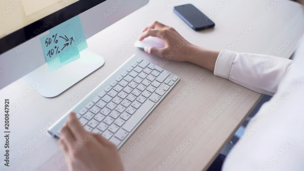Young businessman is working at computer in modern office, sitting at table in business style clothes, 4k touching keyboard, looking at monitor, on wooden desk there is smartphone. Concept: working Young businessman is working at computer in modern office, sitting at table in business style clothes, 4k touching keyboard, looking at monitor, on wooden desk there is smartphone. Concept: working