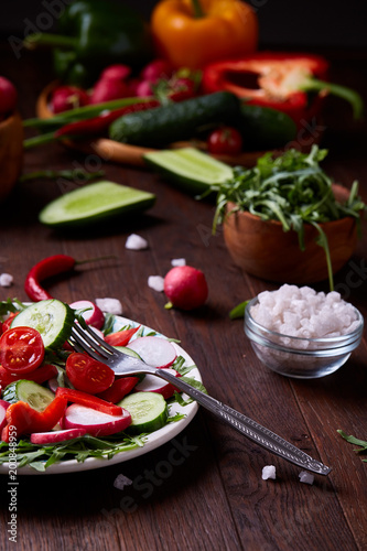 Creative fresh vegetable salad with ruccola, cucumber, tomatoes and raddish on white plate, selective focus