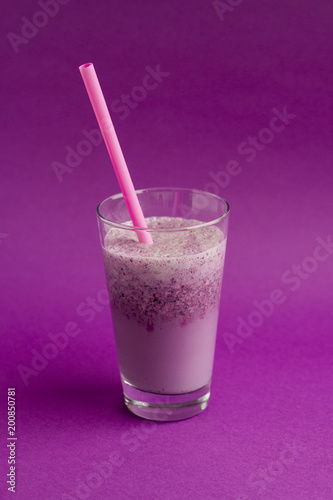 Glass of berry smoothie with straw on purple background. Pink milkshake. Healthy drink. Blueberry cocktail.