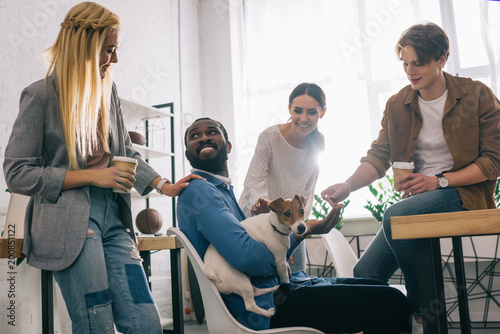 african american businessman sitting with dog surrounded by smiling colleagues