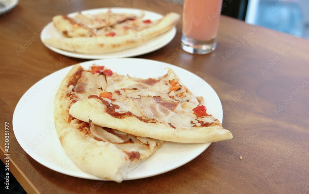 Close-up of pizza slices on a white plate on a wooden table next to a glass of compote. Close-up of pizza slices on a white plate on a wooden table next to a glass of compote.