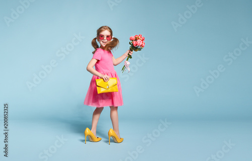 funny child girl fashionista in big mother's shoes on colored background