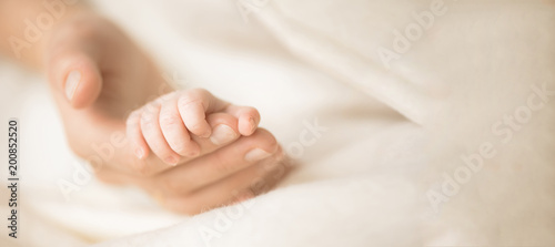 Female hand holding her newborn baby's hand. Mom with her child. Maternity, family, birth concept. Copy space for your text. Banner photo