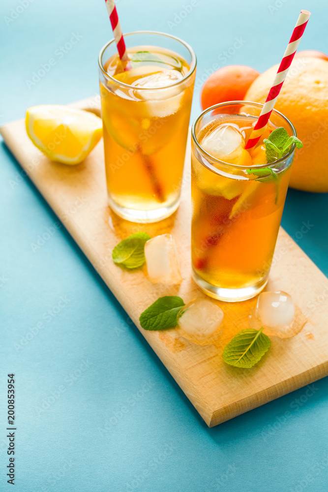 Fototapeta premium Glasses of iced tea with lemon slices and mint on turquoise wooden background