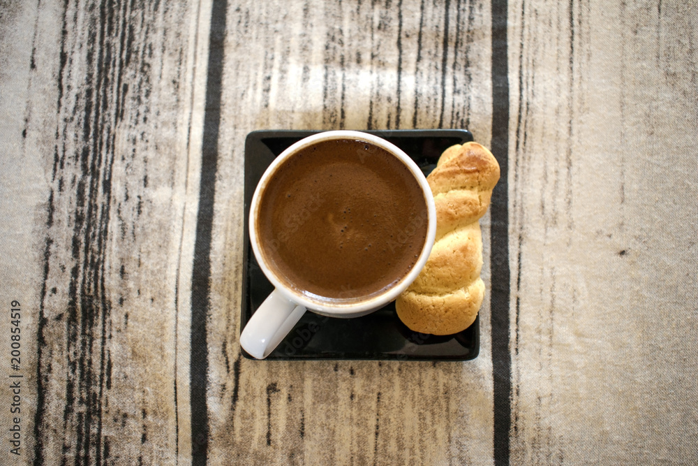 Greek (or Turkish) coffee in a white cup accompanied by a bun Greek (or Turkish) coffee in a white cup accompanied by a bun