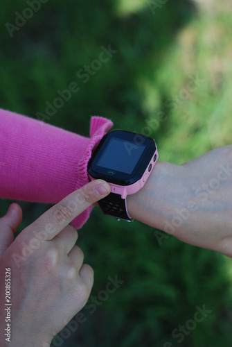 Pink Smartwatch Phone o nLittle girl's Hand. Kid Using pink Intelligent Phone. Summer time Otside.