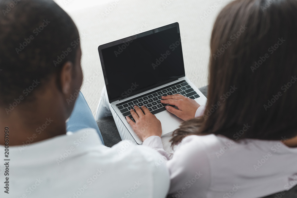 back view of african american couple looking at laptop at home back view of african american couple looking at laptop at home