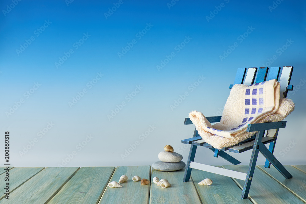 Beach chair on wooden terrace with sea shells, seaside decorations, copy-space on blue background