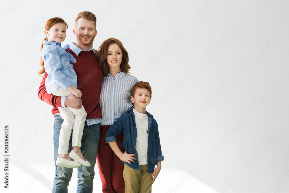 happy redhead family with two children smiling at camera on grey happy redhead family with two children smiling at camera on grey