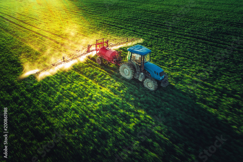 Fotobehang Aerial view of farming tractor plowing and spraying on field