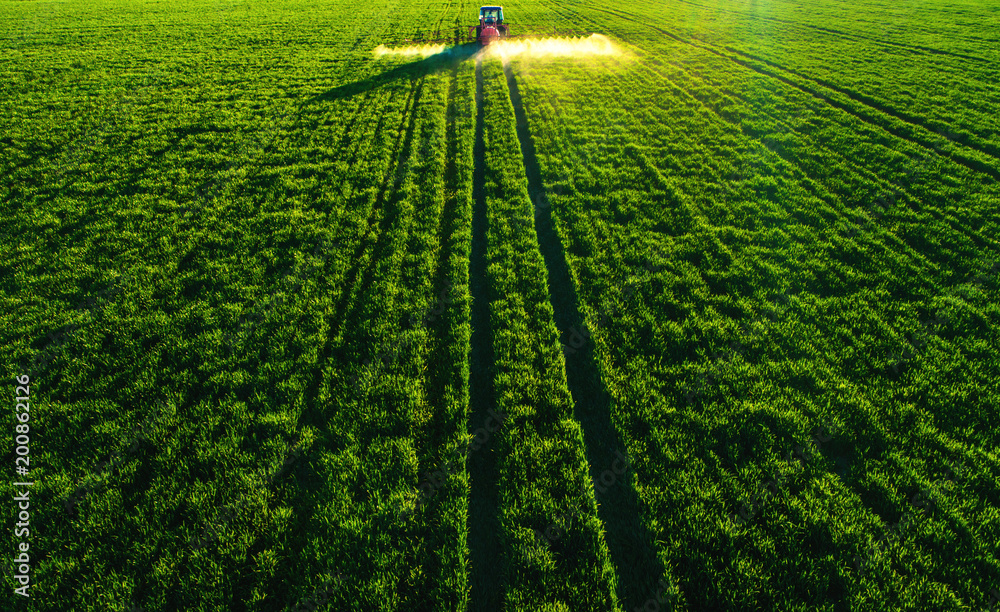 Naklejka premium Aerial view of farming tractor plowing and spraying on field