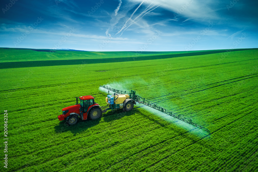 Fototapeta premium Aerial view of farming tractor plowing and spraying on field