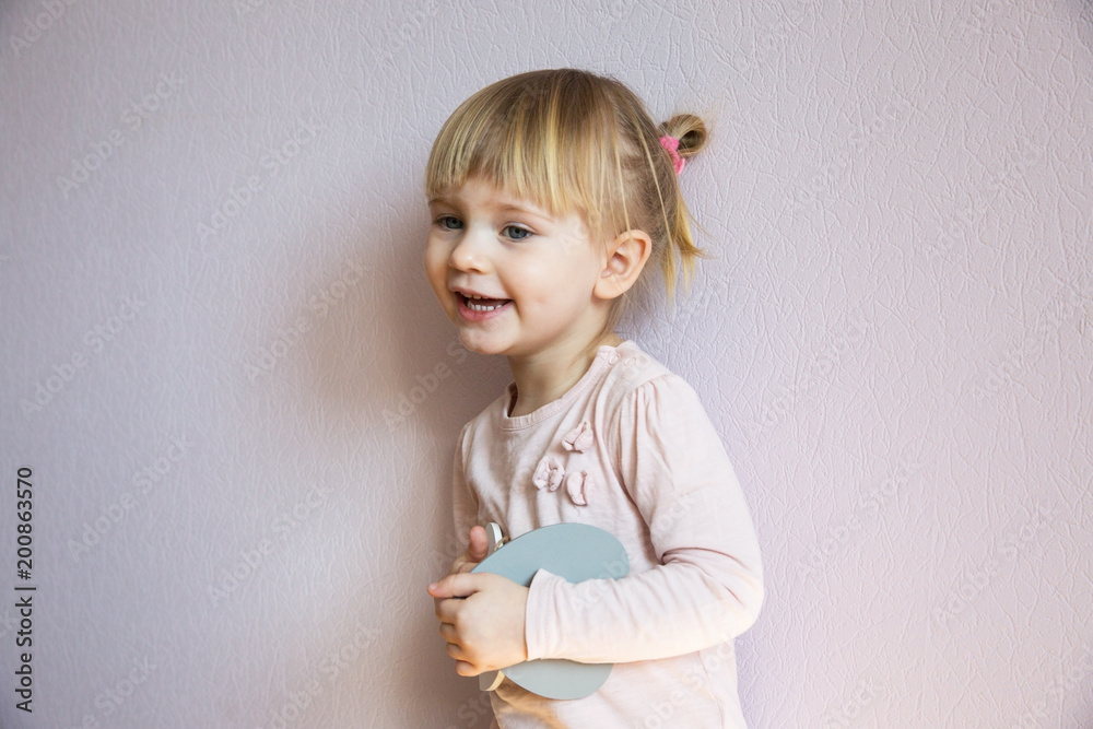Happy little girl. A little girl with blond hair holds two wooden white hearts in her hands, looks at the viewer and laughs. Happy little girl. A little girl with blond hair holds two wooden white hearts in her hands, looks at the viewer and laughs.
