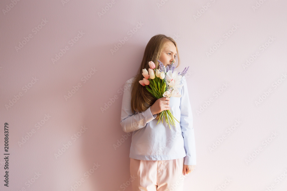 A young beautiful girl with blond dissolved long hair, a felt hat on her head, keeps spring flowers in her hands on a sunny day. Women's Day. A young beautiful girl with blond dissolved long hair, a felt hat on her head, keeps spring flowers in her hands on a sunny day. Women's Day.