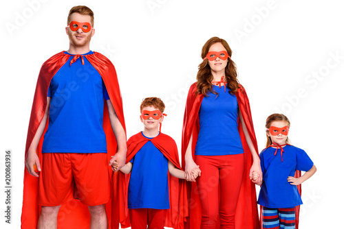 super family in masks and cloaks holding hands and looking at camera isolated on white © LIGHTFIELD STUDIOS
