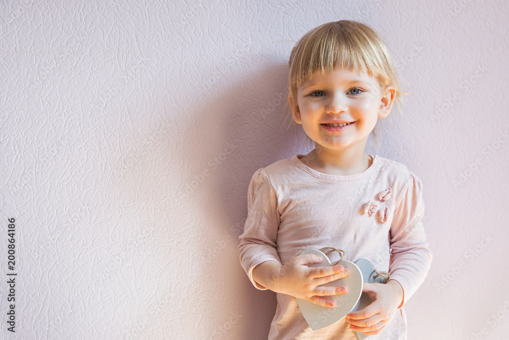 Happy little girl. A little girl with blond hair holds two wooden white hearts in her hands, looks at the viewer and laughs. Happy little girl. A little girl with blond hair holds two wooden white hearts in her hands, looks at the viewer and laughs.