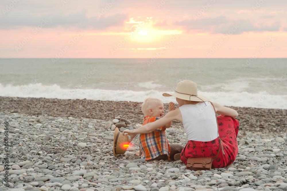 Mom and son play on the pebble beach. Sunset time. Back view