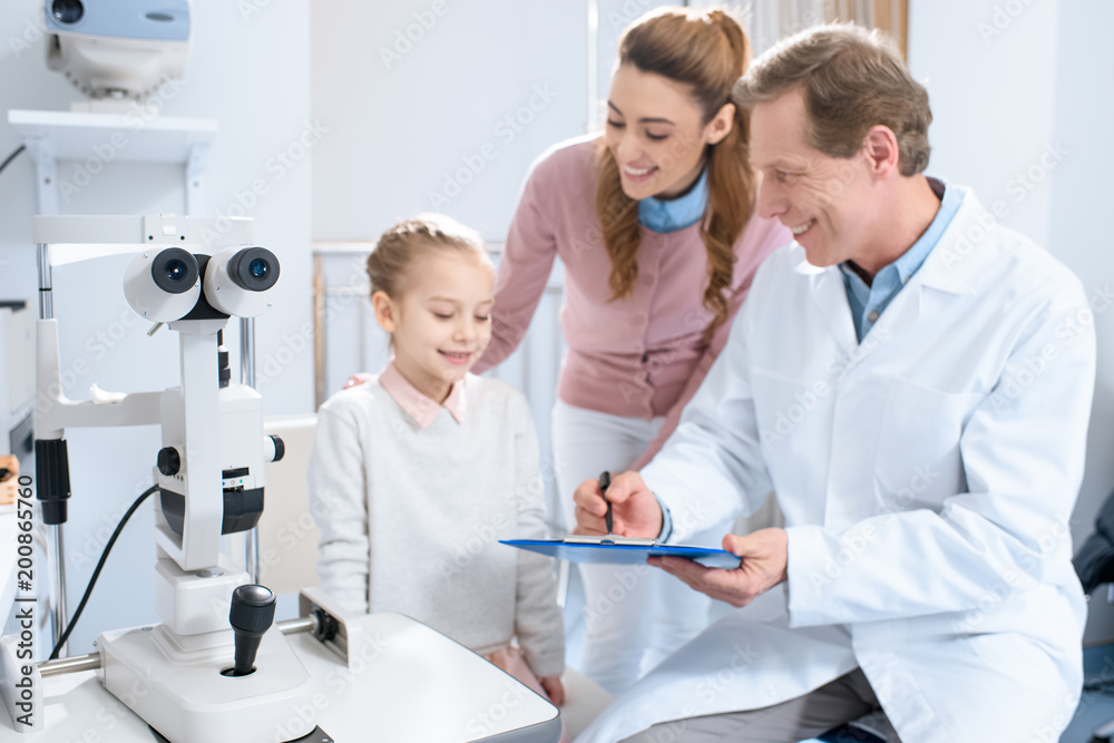 smiling ophthalmologist writing something to patient clipboard in consulting room smiling ophthalmologist writing something to patient clipboard in consulting room