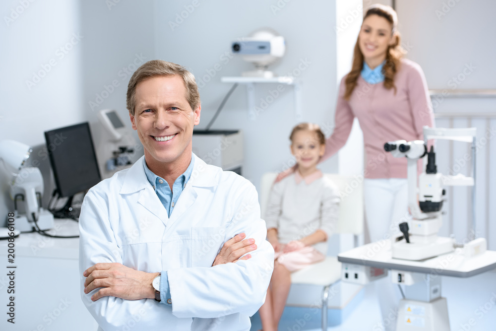 Fototapeta premium smiling ophthalmologist and mother with daughter in consulting room