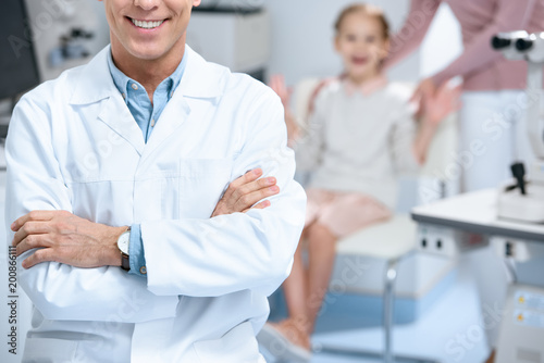 cropped image of smiling ophthalmologist standing with crossed arms in consulting room