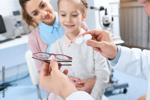 mother and daughter visiting ophthalmologist and choosing eyeglasses or eye lenses in clinic