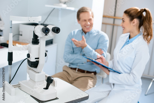 selective focus of optician and man talking with visual field test on foreground