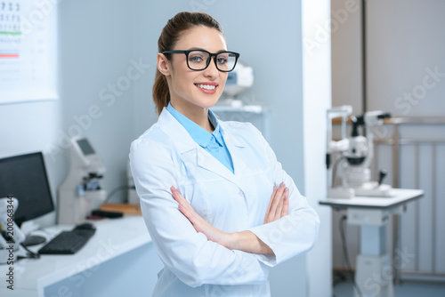 attractive professional ophthalmologist in glasses standing with crossed arms in optical clinic