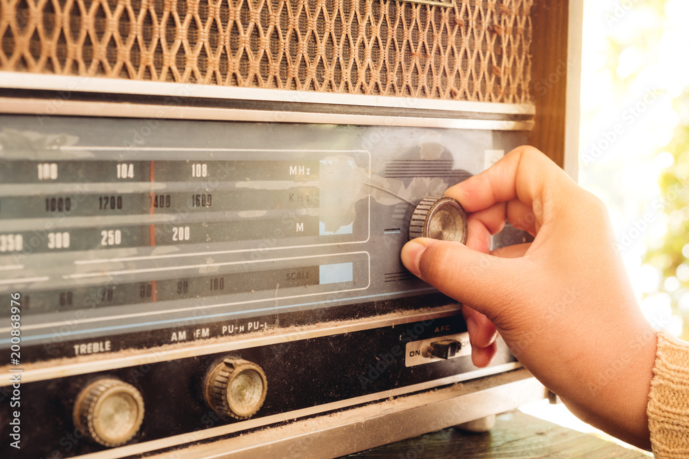 Fototapeta premium Retro styl życia - Kobieta ręcznie dostosowując przycisk rocznika odbiornik radiowy do słuchania muzyki lub wiadomości - efekt tonacji vintage.