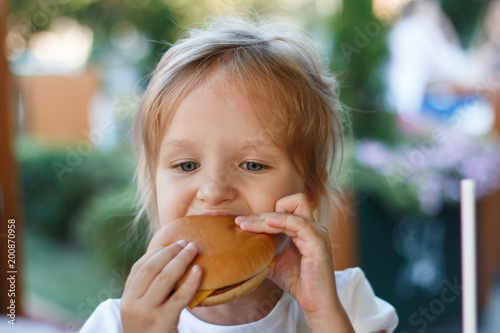 preschool kid girl eats hamburger sitting in cafe