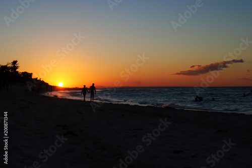 People are holding hands and walking on the beach during sunset. Sunset on the beach in Cuba. Orange sun on the horizon.