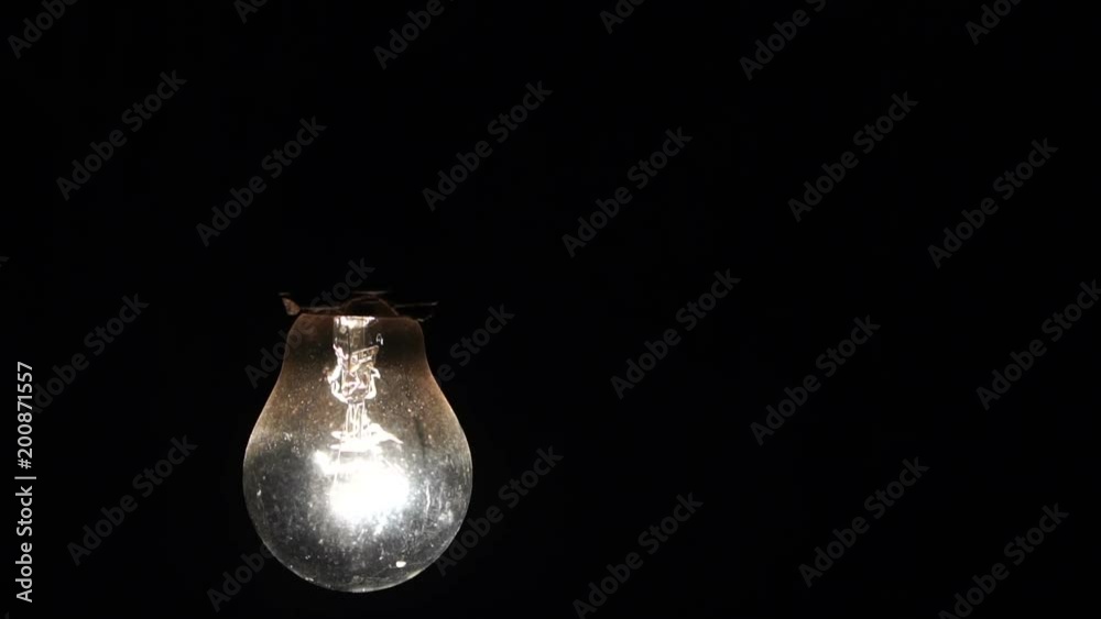 included light bulb slowly swings on the wire. the incandescent lamp is shining in the dark. Slow motion