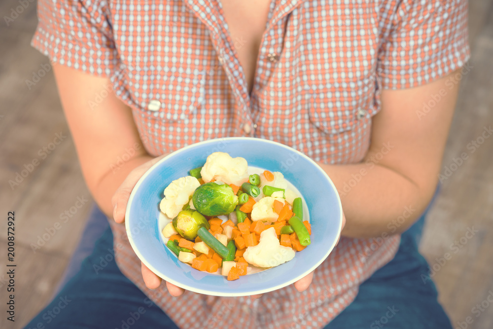 Girl with a plate of vegetables in hands. Healthy eating concept. Proper nutrition. Vegetarian food. Vegans food. Toned image. Girl with a plate of vegetables in hands. Healthy eating concept. Proper nutrition. Vegetarian food. Vegans food. Toned image.