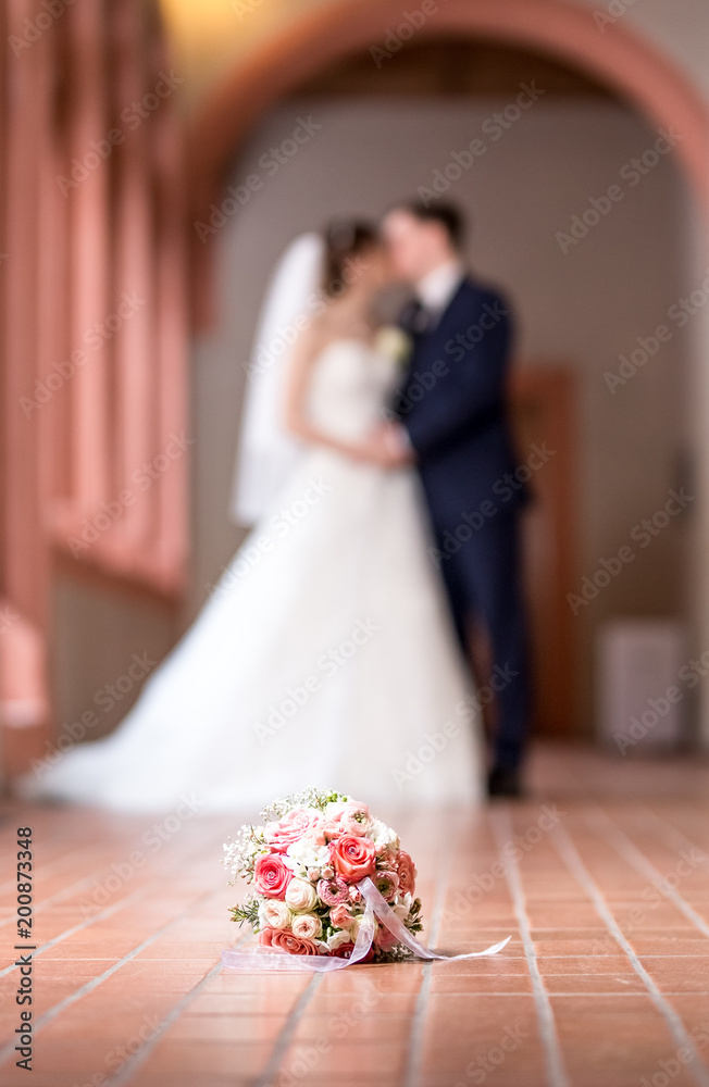 Braut und Bräutigam küssen sich hinter Brautstrauß