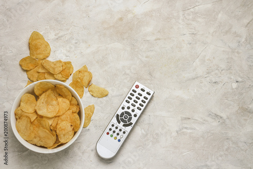 Remote from the TV, Bowl with Chips on a Light Stone Background. The concept of TV viewing and sports tournaments. Flat lay, top view photo