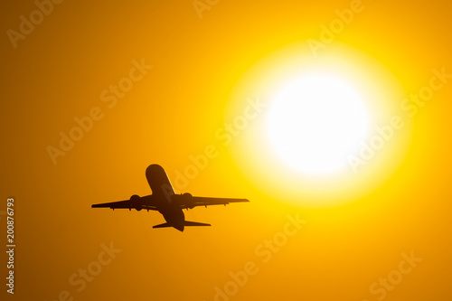 Silhouette of airplane taking off during sunset, flies near the disc of the sun.