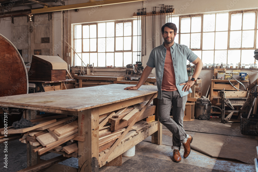 Young carpenter standing by a table in his woodworking shop