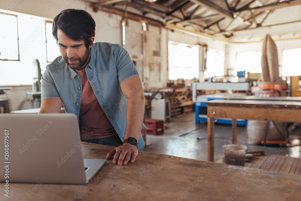 © mavoimages - Craftsman working online with a laptop in his woodworking shop © mavoimages - Craftsman working online with a laptop in his woodworking shop