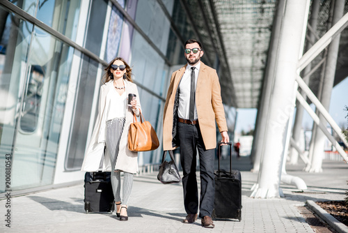 Business couple in coats walking out the airport with luggage during the business trip