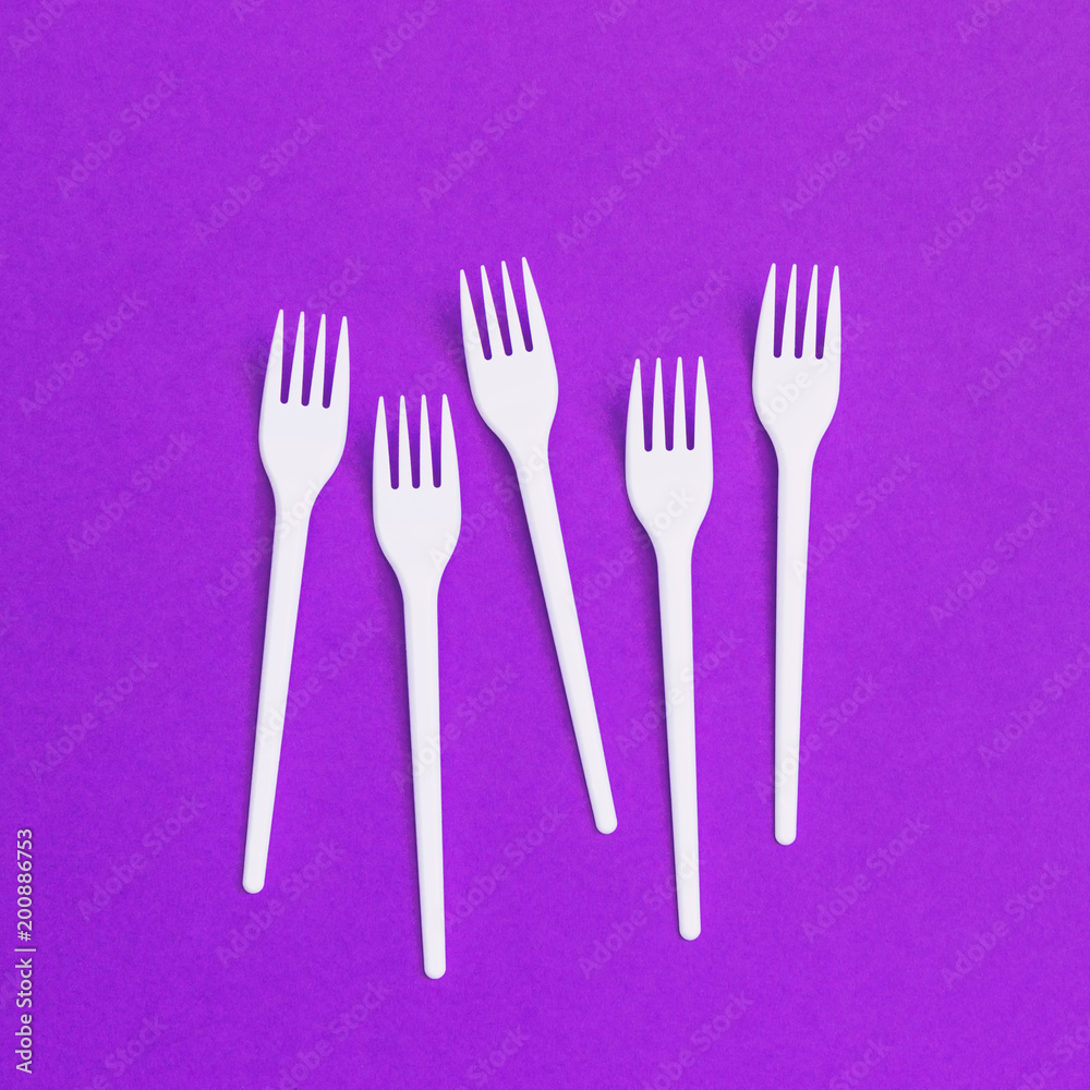 Plastic forks on purple background of paper textures. Minimal flat lay. Creative concept of food and meal Plastic forks on purple background of paper textures. Minimal flat lay. Creative concept of food and meal