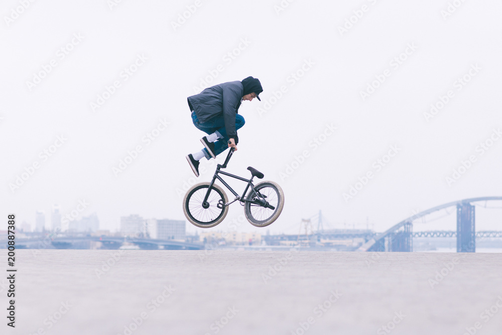 Naklejka premium Young BMX bicycle reader does tricks in the air against the background of the urban landscape. BMX freestyle. Street culture
