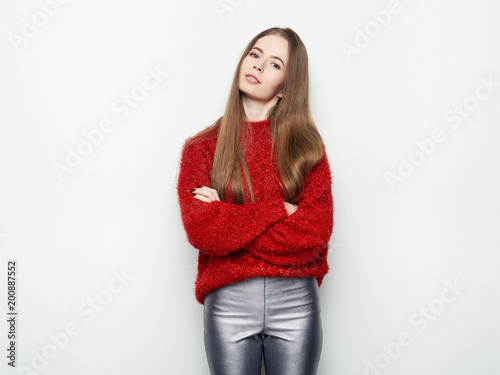 Spectacular blonde woman in red blouse silver leather pants posing in front of white wall. Graceful girl gorgeous long hair having fun on photoshoot.