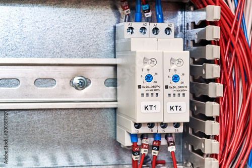 Two time relays with adjustments in the electrical Cabinet. The relays are fixed to the mounting panel. Electric wires or cables are laid in the perforated channel on the right.