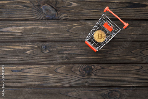a cart from a supermarket, bitcoin on a wooden background. virtual money. the Internet