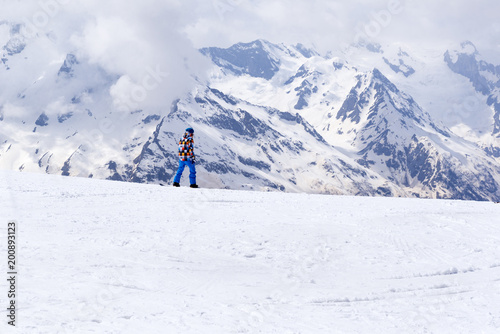 snowboarding rides on the snowy slope of the mountain on the background of mountain slopes and peaks