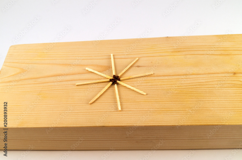 Eight thin matches laid in the form of a star on the treated surface of a wooden board.