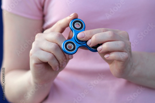 girl in pink t-shirt is playing blue metal spinner in hands on the street, woman playing with a popular fidget spinner toy, anxiety relief toy, anti stress and relaxation fidgets. photo