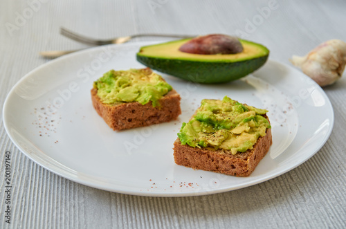 Tasty avocado toasts on the white plate with black salt and garlic. Vegan avocado sandwiches on the gray background with free copy space. Close up view